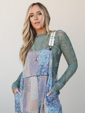 A layered boho look featuring patchwork floral overalls over a sage green lace long-sleeve top — the kind of outfit that feels effortless and intentional at the same time.