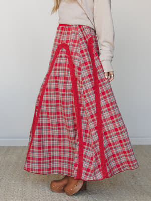 A flowy red plaid maxi skirt styled with a cream textured sweater and tan studded clogs — the kind of outfit that makes a farmer's market feel like a main character moment.