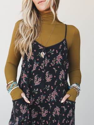A floral jumpsuit layered over a mustard turtleneck — the kind of outfit that looks like it came together effortlessly but was absolutely thought out, finished with stacked bracelets and a long pendant necklace.