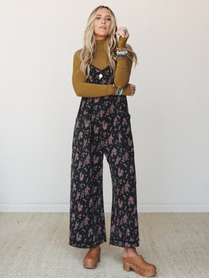A floral wide-leg jumpsuit layered over a mustard turtleneck with wood-heel clogs and a stack of boho jewelry — the kind of outfit that makes a Tuesday feel intentional.