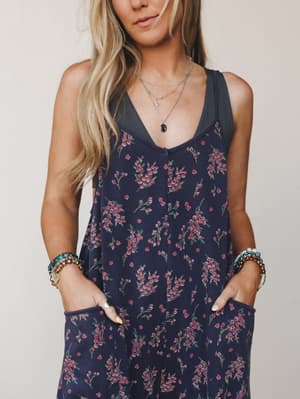 A flowy navy floral jumpsuit with side pockets, styled with layered silver necklaces and stacked beaded bracelets — the kind of outfit that looks like you tried just the right amount.
