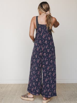 Shot from the back, this wide-leg floral overall jumpsuit in navy has an easy, lived-in feel — styled with leopard platform slides and stacked turquoise bracelets for that effortless boho-everyday energy.