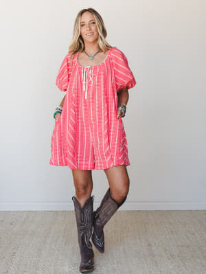A breezy red gingham mini romper with puff sleeves and a lace-up neckline, styled with dark cowboy boots and layered turquoise jewelry for an effortless Western-boho vibe.
