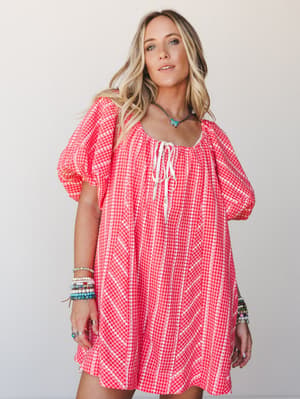 A breezy red gingham mini dress with white floral embroidery stripes and puff sleeves, styled with stacked boho bracelets and a turquoise necklace — the kind of dress that makes a Tuesday feel like a road trip.