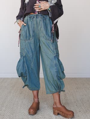 Cropped wide-leg cargo pants in a washed denim finish, styled with a dark linen top, floral accents, and chunky brown clogs — the kind of outfit that looks effortless but definitely took thought.
