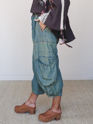 A side-profile shot of a model in wide-leg denim cargo pants with gathered ankles and oversized patch pockets, styled with a layered boho top and wood-platform clogs — the kind of outfit that looks effortless but clearly took some thought.