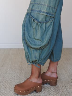 A close-up of balloon-style denim cargo pants in a faded, vintage-washed denim paired with tan studded clogs — the kind of detail shot that makes you stop scrolling.