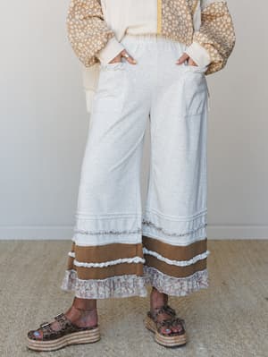Wide-leg cropped pants in light heather gray styled with a floral patchwork jacket — the tiered ruffle hem with a caramel colorblock band and floral ruffle finish gives these the kind of personality that makes people ask where you got them.