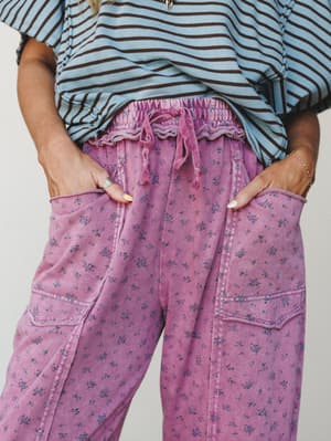 A close-up mid-shot of washed magenta cargo-style pants with an all-over ditsy floral print, styled with a blue and brown striped top — the kind of outfit that looks effortless but is clearly very much on purpose.