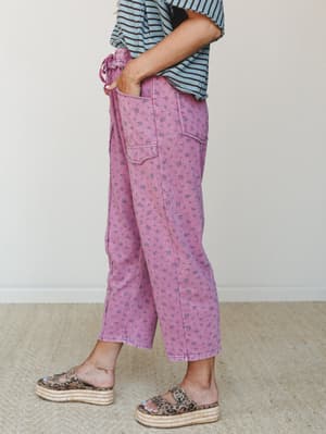 A side-profile shot of wide-leg cropped pants in a washed magenta with an all-over ditsy floral print, styled casually with a striped tee and leopard print platform sandals — the kind of outfit that looks effortless but definitely was not an accident