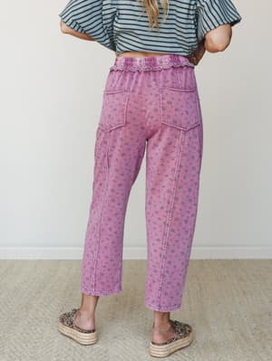 A back-view shot of relaxed, cropped floral pants in a washed magenta with a ruffled elastic waist and patch pockets, styled with a striped crop top and leopard espadrilles for an effortlessly playful everyday look.