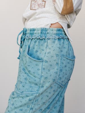 A close-up detail shot of wide-leg floral cargo pants in a faded teal blue, paired with a casual graphic tee — the kind of pants that feel like a personality, not just a bottom.
