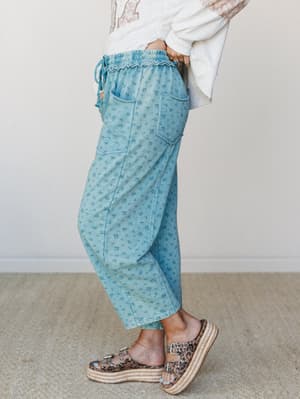 A side-profile shot of cropped floral jogger pants in faded teal, styled with an oversized graphic sweatshirt and platform espadrille sandals — the kind of outfit that makes errand-running feel like a personality.
