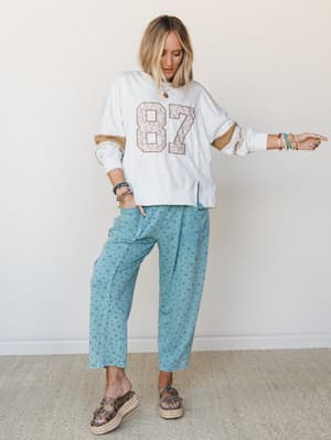 A relaxed, lived-in outfit pairing a floral-patched varsity sweatshirt with roomy teal floral pants and platform espadrille sandals — the kind of look that feels effortless but clearly thought through.