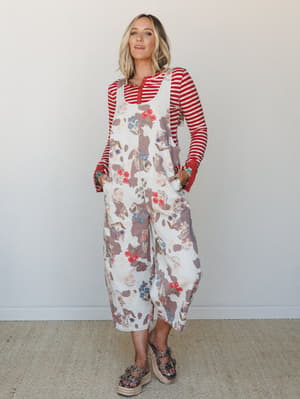A wide-leg floral and cow-print jumpsuit layered over a red striped long-sleeve top — the kind of mix-and-match that looks effortless but was definitely thought about, styled with platform studded sandals against a clean studio wall.