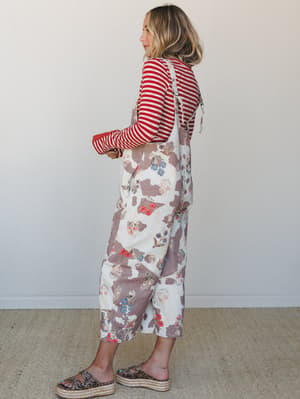 A model shot in profile wearing a wide-leg floral jumpsuit over a red striped long-sleeve top, styled with platform espadrille sandals — the kind of layered, expressive outfit that looks effortless but was absolutely thought about.