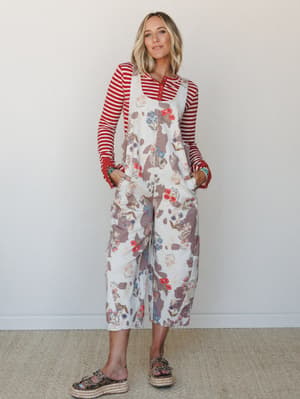 A floral and cow-print patterned wide-leg overall jumpsuit layered over a red striped long-sleeve top — the kind of outfit that looks effortlessly assembled but absolutely wasn't an accident.