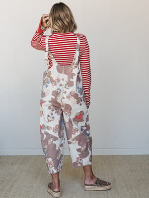 Shot from behind, a model wears wide-leg floral overalls over a red striped long-sleeve top — the kind of outfit that looks like it came together effortlessly but clearly didn't happen by accident.