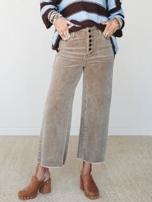 Wide-leg corduroy pants in a faded warm taupe are styled with a chunky stripe sweater, clogs, and stacked boho jewelry — the kind of outfit that looks effortless but was definitely thought about.