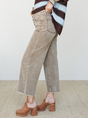A side-angle shot of wide-leg corduroy trousers in a warm tan paired with a striped crochet sweater and studded heeled clogs — the kind of outfit that looks like it came together effortlessly but definitely did not.