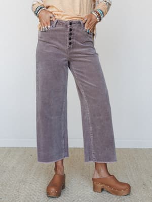 Wide-leg corduroy trousers in a washed dusty lilac styled with a peach long-sleeve top, stacked bead bracelets, silver rings, and chunky brown clogs — the kind of outfit that looks effortless but was absolutely thought through.