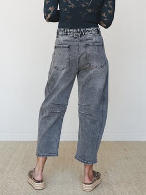 Shot from behind, a model pairs acid-washed wide-leg denim in faded charcoal with a black lace long-sleeve top and leopard espadrille flatforms — relaxed and a little rock-and-roll.