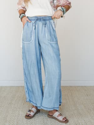Wide-leg chambray pants with a soft, worn-in wash styled with a white crop top, stacked beaded bracelets, and slide sandals — the kind of outfit that looks effortless but is definitely intentional.