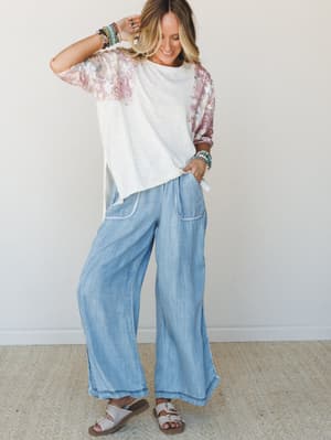 A relaxed, sun-washed outfit moment — wide-leg chambray pants paired with a colorblock floral top, sandals, and a stack of boho bracelets that look like they've been collecting since forever.