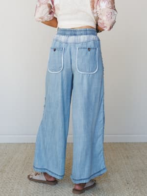 Shot from behind, these wide-leg chambray pants have an easy, lived-in feel — elasticized waist, patch pockets with contrast braided trim, and a relaxed silhouette that reads effortlessly boho paired with a floral top and sandals.