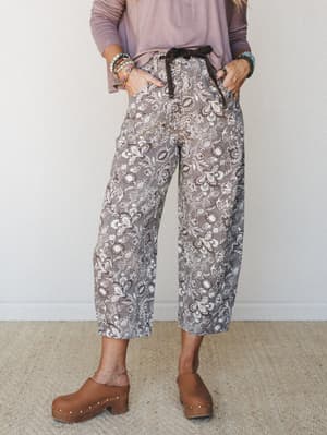 A cropped barrel-leg pant in a mocha floral print styled with a dusty lavender long-sleeve top, wood-studded clogs, and stacked beaded bracelets — the kind of put-together-but-effortless outfit that looks like it came naturally.