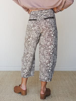 A back-view shot of wide-leg cropped floral pants in a warm mocha tone, styled with a blush long-sleeve top and wood-studded clogs — the kind of outfit that looks effortless but was definitely thought about.