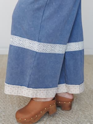 A close-up detail shot of wide-leg denim jumpsuit hems styled with tan studded clogs — the lace trim inset and floral ruffle hem peek are the kind of details you notice up close and never stop loving.