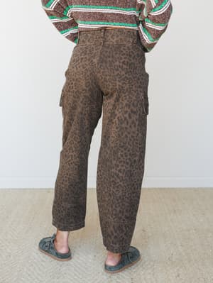 Shot from behind, a model wears wide-leg leopard print cargo pants in a warm brown paired with a striped knit sweater — earthy, expressive, and the kind of outfit that makes a statement without trying too hard.