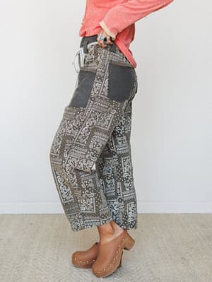 A side-profile shot of wide-leg cropped pants in an earthy olive bandana patchwork print, styled with a coral waffle knit top and tan studded clogs — the kind of outfit that looks effortless but clearly wasn't an accident.