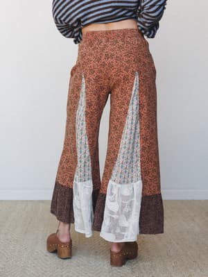 Shot from the back, these wide-leg flare pants in rust floral ditsy print feature contrasting patchwork insets — a geometric medallion panel and lace hem detail — styled with a striped long-sleeve and wood-platform clogs for a very intentional, very