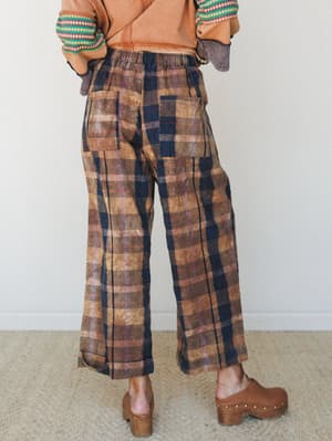 Shot from behind, a model in wide-leg plaid pants with an acid-washed, earthy finish pairs them with a rust cropped sweatshirt and brown clogs — the kind of outfit that feels thrown together in the best possible way.