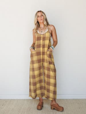 A wide-leg plaid jumpsuit in golden yellow and warm brown worn with stacked boho jewelry and wood-platform clogs — relaxed, earthy, and effortlessly 70s without trying too hard.