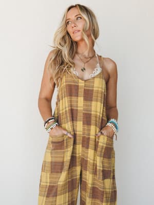A relaxed wide-leg jumpsuit in golden yellow plaid worn with layered boho jewelry and a peeking lace bralette — the kind of outfit that looks effortless but was definitely thought about.
