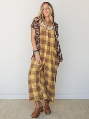 A wide-leg plaid jumpsuit in golden yellow and warm brown is layered under a fringed knit vest, styled with clogs and stacked jewelry for a full-on boho-fall look that feels effortless rather than assembled.