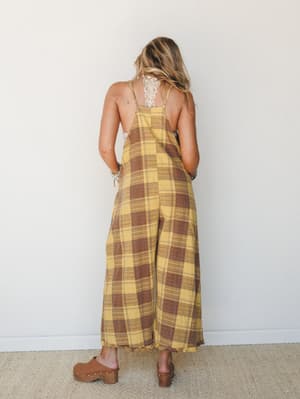 Shot from the back, a wide-leg plaid jumpsuit in golden yellow and warm brown pairs with a lace bralette and wooden clogs — the kind of effortless fall outfit that looks like it was thrown on and somehow landed perfectly.