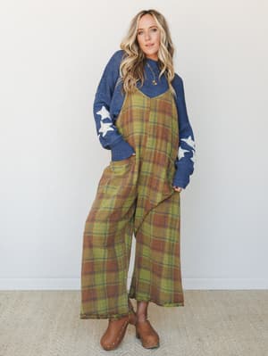 A wide-leg plaid jumpsuit in olive and rust layered over a denim-blue star-print sweater, styled with tan clogs — the kind of effortless fall outfit that looks like it came together by accident but absolutely didn't.
