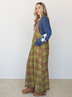 A plaid wide-leg jumpsuit in olive and rust layered over a denim blue star-patch sweater, styled with studded clogs — the kind of put-together-but-effortless outfit that looks like it came naturally.