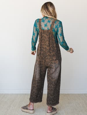 Shot from behind, this outfit pairs wide-leg leopard print overalls in worn brown with a sheer teal floral mesh top underneath — layered, expressive, and the kind of combo that looks effortless but absolutely wasn't an accident.