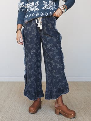 Wide-leg cropped pants in dark denim with an allover delicate floral print, styled with a rose-pattern knit sweater and wood-platform clogs — the kind of outfit that looks effortless but absolutely wasn't an accident.
