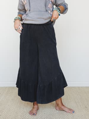 Wide-leg ruffle-hem pants in washed black styled with a floral embroidered hoodie and stacked turquoise jewelry — the kind of effortless, expressive outfit that looks like you tried just enough.
