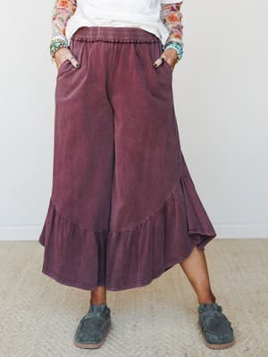 Wide-leg ruffle-hem pants in a washed mulberry worn with a white tee, floral mesh sleeves, stacked turquoise bracelets, and suede loafers — the kind of outfit that looks effortless but is clearly thought out.