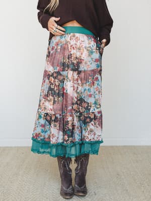 A tiered floral patchwork maxi skirt styled with a cropped dark brown sweater and cowboy boots — the kind of outfit that looks like it came together effortlessly but definitely did not.