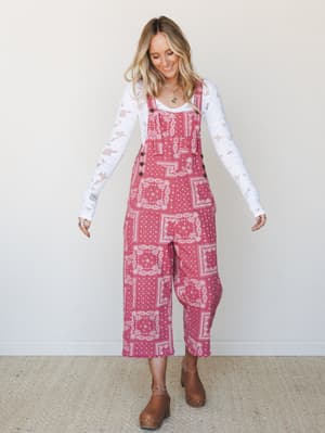 A bandana-print wide-leg overall in rosy pink is layered over a white eyelet long-sleeve top and styled with wood-platform clogs — the kind of outfit that feels effortless but clearly wasn't an accident.