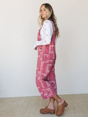 A relaxed, full-length bandana-print overall layered over a white lace long-sleeve top, styled with wood-heel clogs — the kind of outfit that feels intentional without trying too hard.