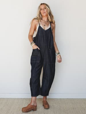 A relaxed dark denim jumpsuit styled with a lace-trim cami underneath, wood-soled clogs, and a stack of beaded bracelets — effortlessly lived-in and the kind of outfit that looks like you tried just enough.